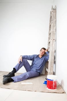 Thoughtful mature man sitting on floor with paint bucket beside