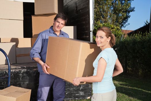 Portrait of couple carrying cardboard box while moving into new home
