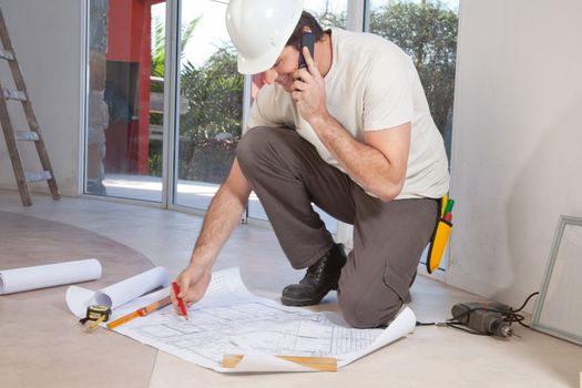 Construction worker working on blueprint and talking on cellphone