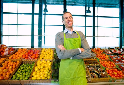 A grocery store owner standing in front of vegetables and fruit