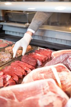 Hand of assistant picking meat in the supermarket at a fresh meat counter