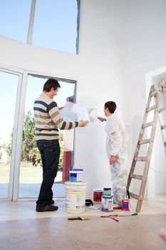 Man going through house plan while painter painting the wall