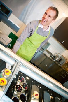 A store clerk selling fresh deserts behind a glass cooler