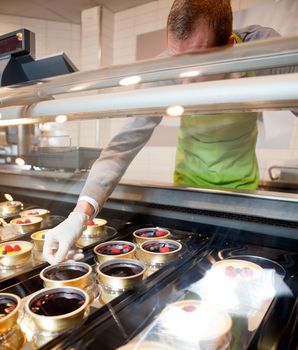 A fresh gourmet desert counter in a store with faceless chef