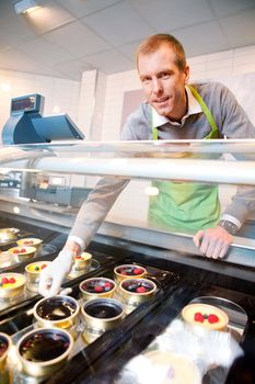 A store clerk selling fancy deserts from a glass counter
