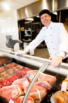 A butcher standing behind a fresh meat counter smiling at the camera