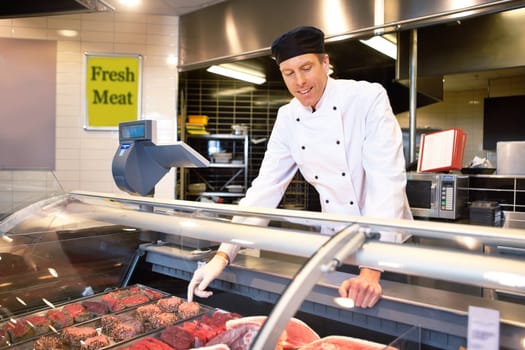 Butcher at a fresh meat counter helping customers