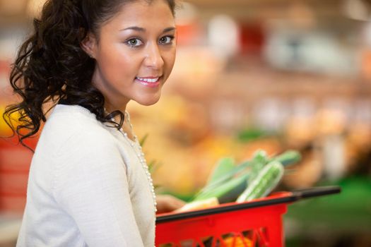 Close-up of young woman with red basket in supermarket and looking at camera