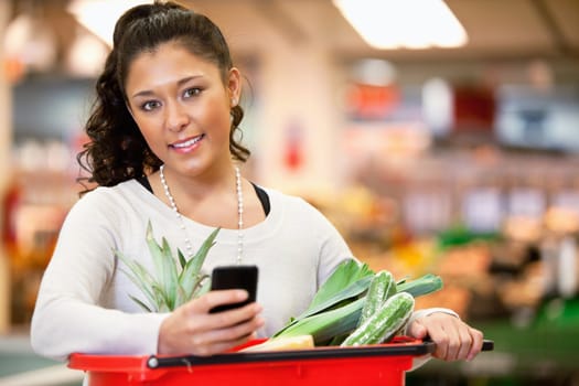 Smiling young woman using mobile phone while shopping in shopping store and looking at camera