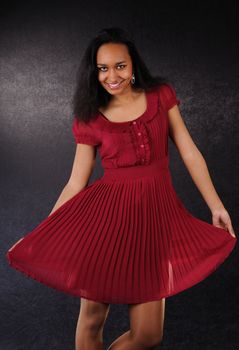 Attractive dancing and smiling young woman in red dress on black background