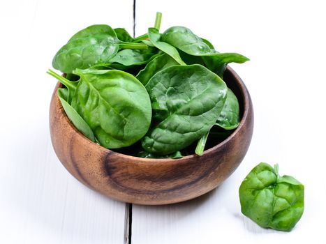 Wooden bowl of spinach on white table