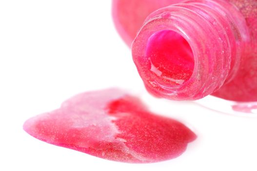 Close-up of open nail polish bottle and poured rose polish on white background. Shallow depth of fields. Focus on bottleneck.