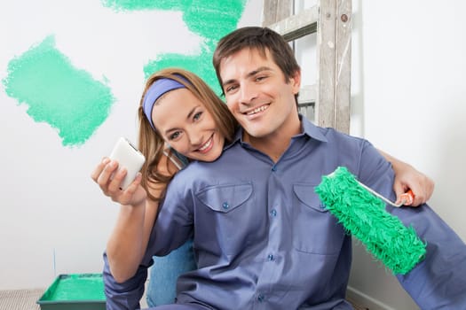 Portrait of smiling couple holding mobile phone and color roller
