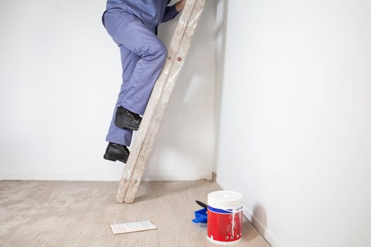 Low section of man's legs climbing wooden ladder