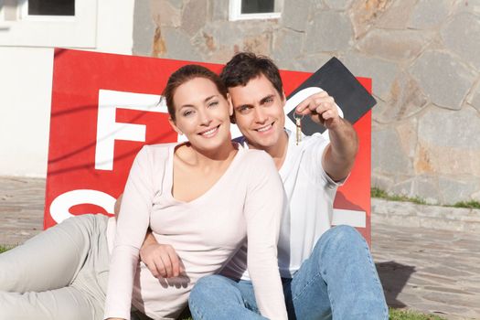 Portrait of smiling man holding keys with wife sitting on side