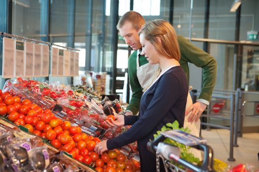 Woman holding tomato while standing with shop worker in grocery store