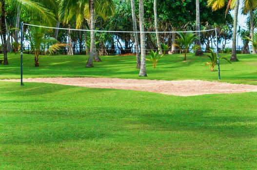 Tropical vacation resort with volleyball court, palm trees and green grass. Focus on the front grass.