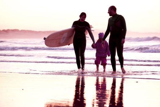 Female surfer and her familly walking in the beach at the sunset