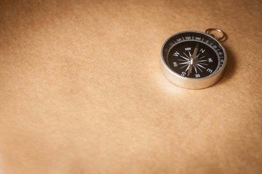 A silver compass with black face pointing north on a brown paper background.