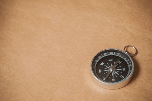 A silver compass with black face pointing north on a brown paper background.