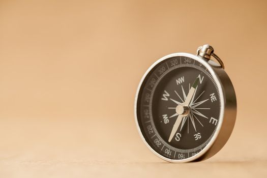 A silver compass with black face pointing north on a brown paper background.