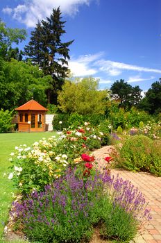 Beautiful garden with blooming roses, brick path and a small gazebo