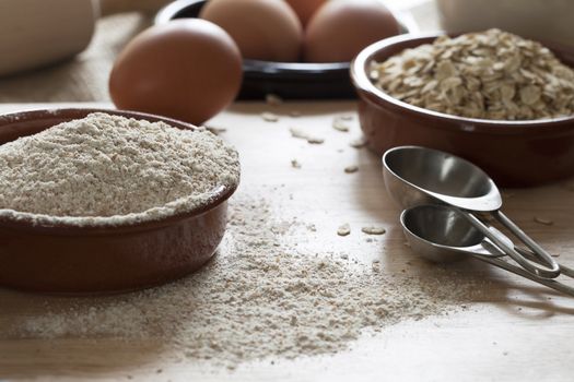 Bowl of whole wheat flour and rolled oats with measuring spoons and eggs in background