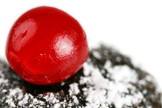 Macro of yummy sweet delicious Maraschino cherry on top of dark chocolate cake with powdered sugar icing; great dessert background with copy space.