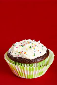 Delicious chocolate cupcake topped with  cream cheese frosting and colorful candy over red background for copy space.