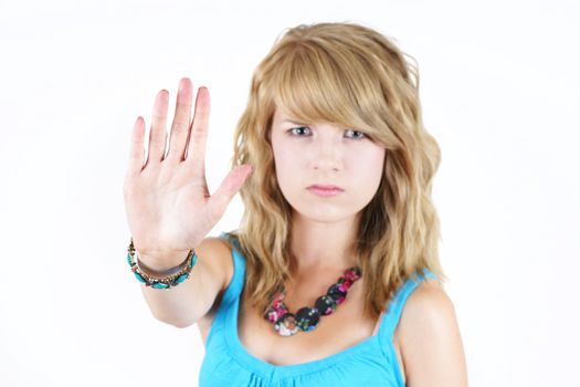 Young blond teenager girl with sad or angry face raising her hand to say NO or STOP, strong concept against drugs, violence, abuse or others: focus on hand in forefront.