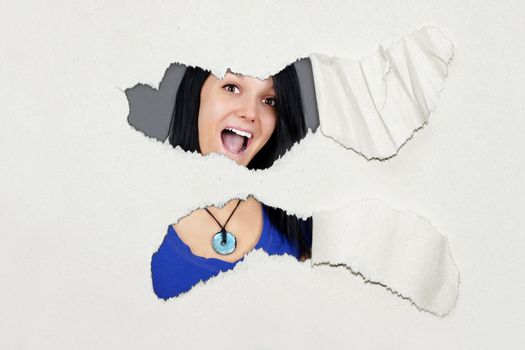 Very surprised young woman under ripped thick textured paper, fun advertisement.