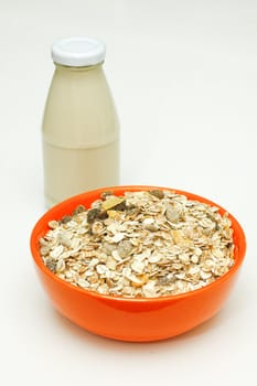 Orange bowl of cereal with a glass bottle of  milk.