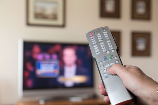 Silver TV remote control being pressed by lady with TV in background