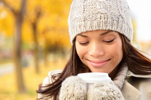 Fall woman drinking coffee in autumn city park. Girl enjoying hot drink from disposable coffee cup. Fall lifestyle concept with beautiful young mixed race Chinese Asian / Caucasian female model.
