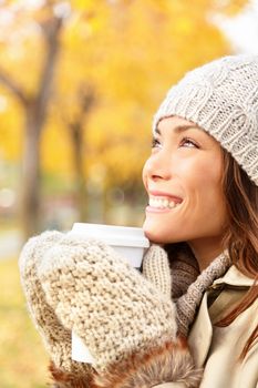 Autumn woman drinking coffee. Fall concept of young woman enjoying hot drink from disposable coffee cup outdoors in fall landscape. Serene happy mixed race Asian / Caucasian female model in Autumn in city forest park.