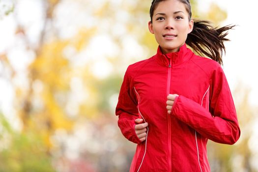 Woman runner running in autumn forest. Young mixed race girl jogging in fall colors.