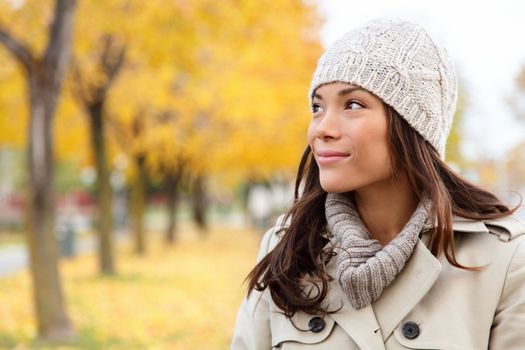 Fall woman portrait of woman looking sideways smiling serene. Beautiful young multiracial woman walking in autumn in city forest park in trench coat.
