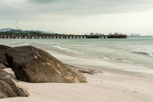 Big stone in sand on beach with jetty and cloud in evening time