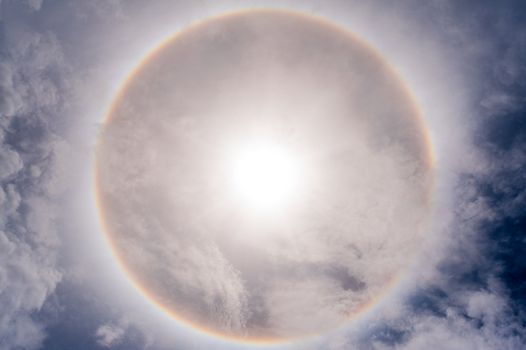 Sun with circular rainbow sun halo in sky with cloud