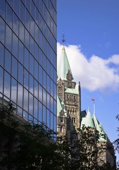 The canadian Parliament Confederation building seen behind a modern glass building in Ottawa, Canada.