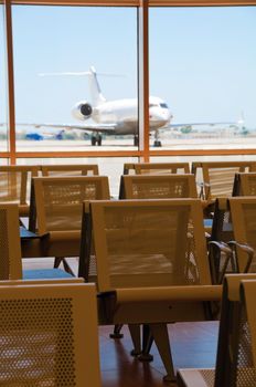 Seats in airport for waiting with parked business plane on background. Focus on the seat.