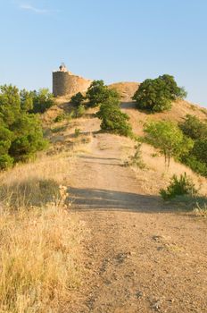 Pathway to ruins of a watch tower between dry grass and green trees