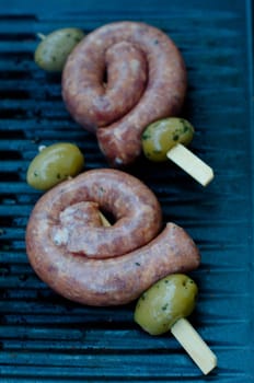 Italian salsiccia sausage skewers garnished with olives being grilled on BBQ