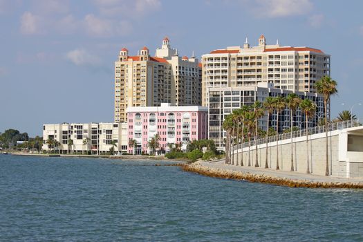 View of buildings on the edge of  Sarasota Bay, Sarasota, Florida from the water with palm trees, blue sky and clouds.