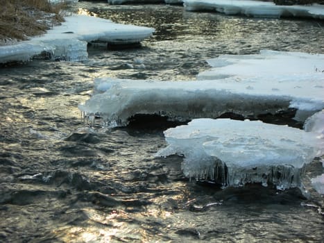 Flowing water in a brook is covered by clear ice