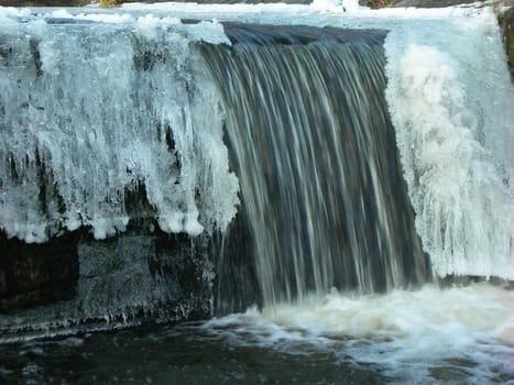 Flowing water in a brook is covered by clear ice