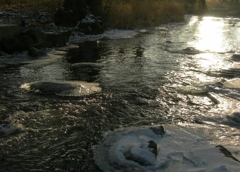 Flowing water in a brook is covered by clear ice