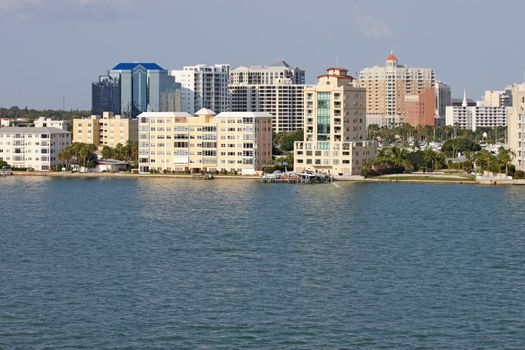 View of buildings on the edge of  Sarasota Bay, Sarasota, Florida from the water with palm trees and a blue sky.