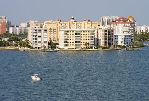 View of buildings on the edge of  Sarasota Bay, Sarasota, Florida from the water with a small pleasure boat, palm trees and blue sky.
