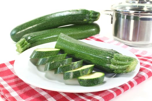 fresh sliced zucchini on a plate with pot in front of light background